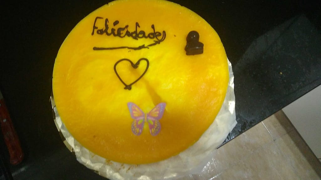 una tarta redonda de mousse de mango decorada, con felicidades de chocolate y una mariposa comestible