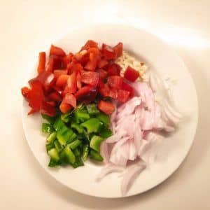 En un plato blanco cortadas cebolla,ajos y pimiento rojo y verde