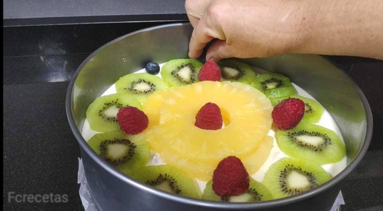decorando la tarta con frutas, piña, kiwi ,frambuesas y arándanos