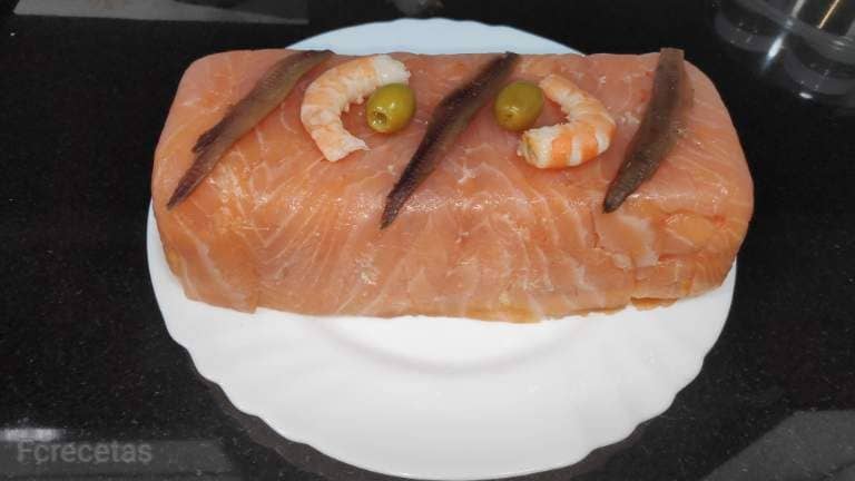 un pastel frío de salmón decorado con gambas y anchoas