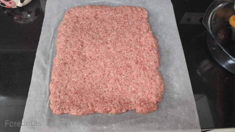 una capa de carne picada sobre papel de hornear