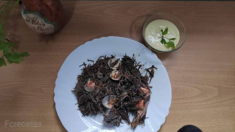 un plato de fideuá negra con su salsa allioli
